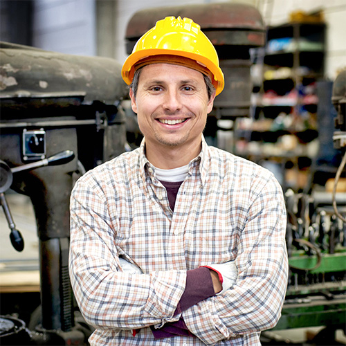 Owner of a business with his arms crossed and a yellow hard hat on his head.